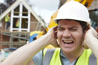 man with hard hat on building site holding his ears